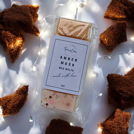 A close up of Amber Musk fragranced Wax Melt from Touch of Class.  The wax melt is snap bar shaped with white, gold and sunset glitter.