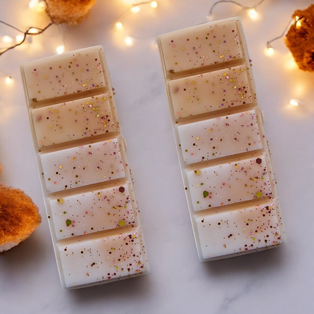 A close up of Amber Musk fragranced Wax Melt from Touch of Class.  The wax melt is snap bar shaped with white, gold and sunset glitter.