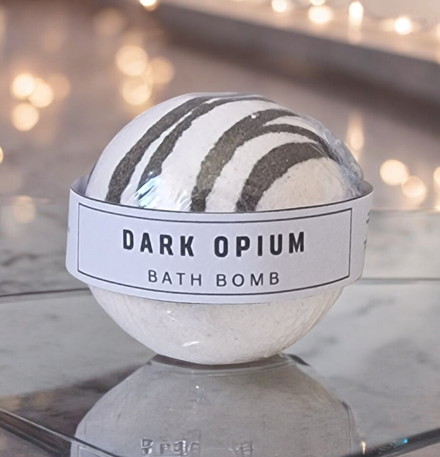 Close-up photo of a Dark Opium bath bomb by Touch of Class.  The bath bomb is round in shape.  The bath bomb is white and gold